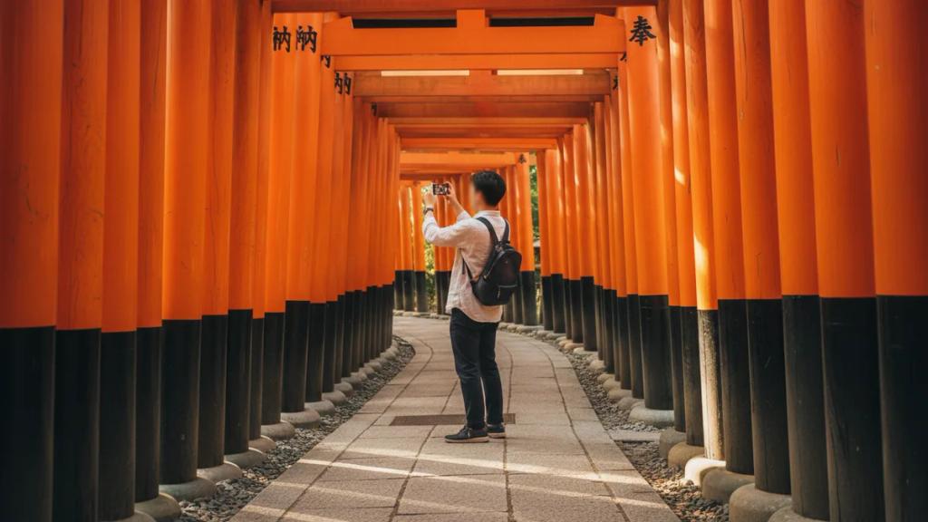 Traveller checking a phone in front of a traditional wooden temple gate at golden hour