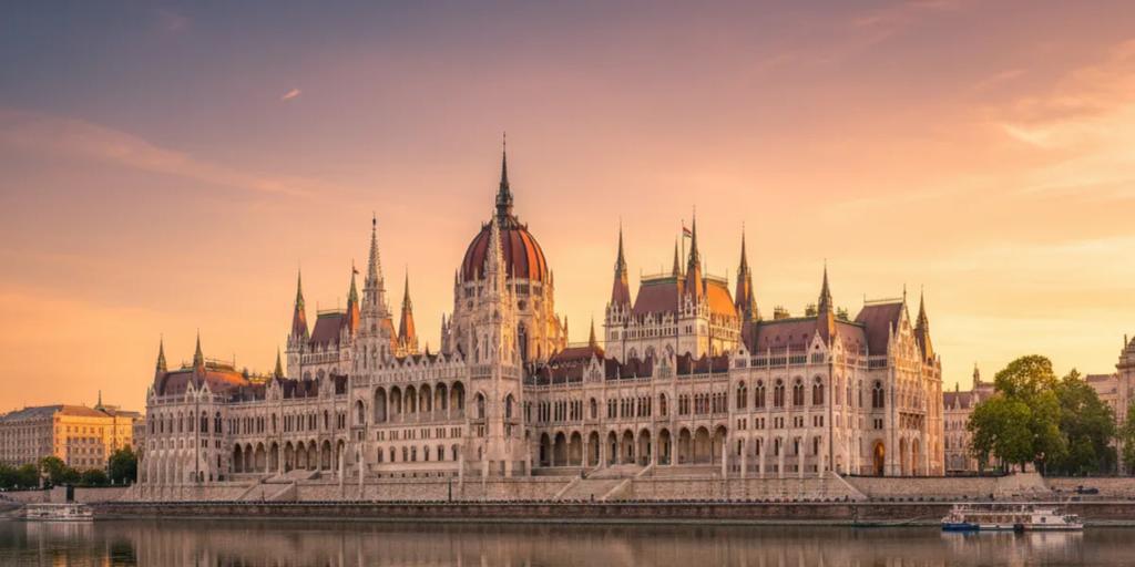 The Hungarian Parliament glowing over the Danube at blue hour, seen from the Buda side