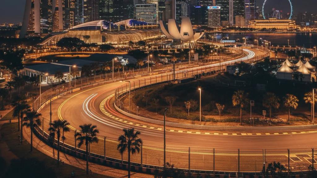 Formula 1 cars racing under floodlights on the Marina Bay street circuit with the Singapore skyline behind